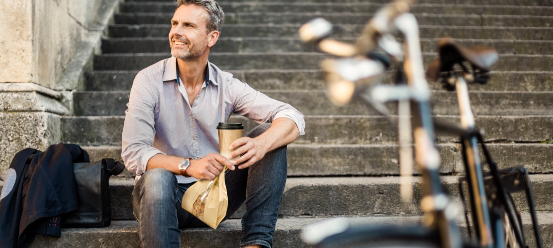 Man on stairs with cup of coffee and bread bag